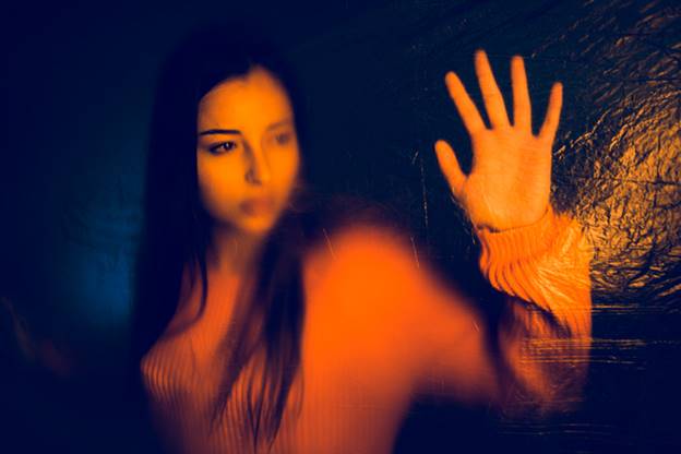 A blurry image of a woman with her hand against a pane of glass, with orange and blue lighting. This image may be used to illustrate content messaging on a website.